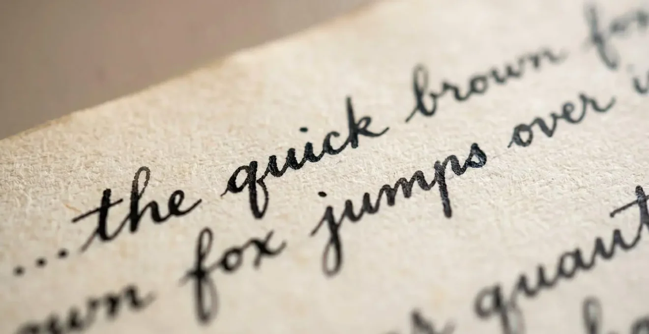 Gros plan sur une page de papier vieilli couverte d'une écriture manuscrite élégante à l'encre noire, lumière naturelle rasante révélant la texture du grain