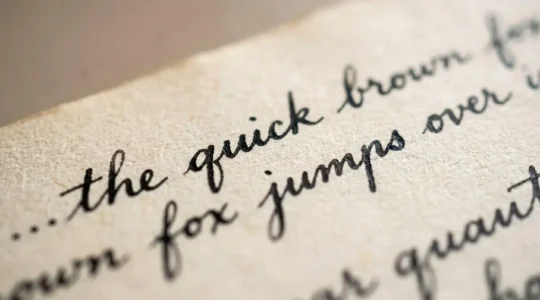 Gros plan sur une page de papier vieilli couverte d'une écriture manuscrite élégante à l'encre noire, lumière naturelle rasante révélant la texture du grain
